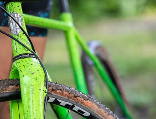 Close-up of the All-City head badge on the green Nature Boy and a muddy WTB Cross Boss tyre.
