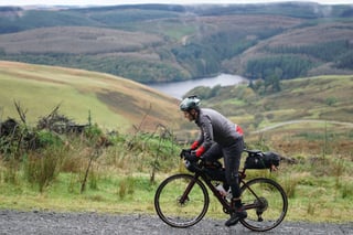 Rider in a green helmet on a gravel track across open moorland above a reservoir on the Wildcat 100 route in Mid Wales.