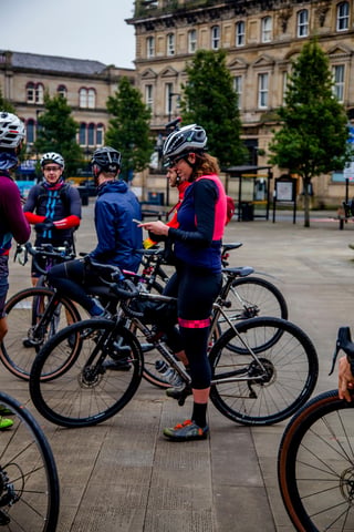 Emma checks her phone among a group of riders and gravel bikes gathered in a town square before the PennDURO.