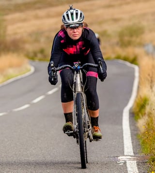 Emma rides the Kinesis Tripster V3 along a moorland road, Coefficient Wave handlebars curving up at the hoods.