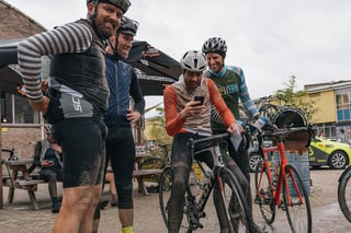 Mud-splashed riders crowd round a phone after the Backyard Breakaway, one still astride a Scott bike.