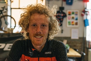 Curly-haired rider with a mud-flecked face and jersey sits in the Cyklist cafe after the Backyard Breakaway.
