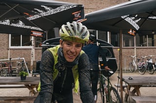 Wallonie-Bruxelles rider in a muddy lime Adeps gilet smiles under cafe parasols after the Backyard Breakaway.
