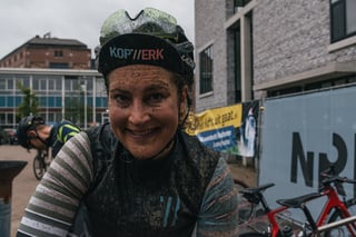 Grinning rider with a mud-covered face and gilet after finishing the Scope Backyard Breakaway in Eindhoven.