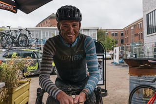 Rider in a muddy Kopwerk jersey grins from the saddle at the finish of the Backyard Breakaway.