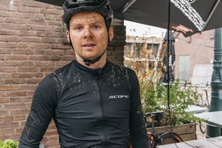 Mud-spattered rider in a black Scope jersey and helmet under a cafe parasol after the Backyard Breakaway.