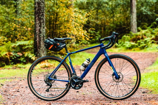 Blue carbon Salsa Warroad with a saddle pack and tan-wall tyres, side view on a forest track.