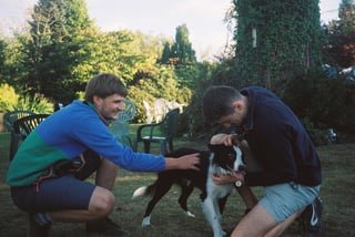 Two people crouch to stroke a black and white border collie on the lawn at the weekender's base.