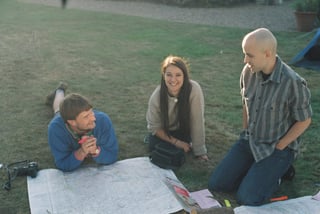 Three riders plan routes around paper maps spread on the grass at the Low Key Lakes Weekender campsite.