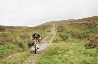 Mountain biker splashes through a stream crossing a stony moorland track in the Lake District.