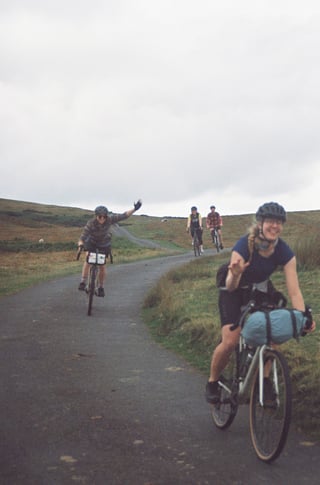 Four riders smile and wave along a quiet Lake District lane during the Low Key Lakes Weekender.