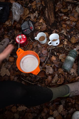 Daypacking kit from above on autumn leaves: Primus gas canister, orange collapsible bowl, two enamel mugs and a bottle.