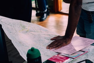 Hand resting on a paper map beside the Zetland Cycles Low Key Lakes Weekender checkpoint sheets.