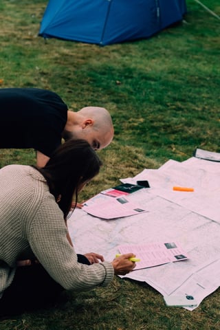 Two riders crouch over a paper map with a highlighter on the lawn beside a tent at the Low Key Lakes Weekender.