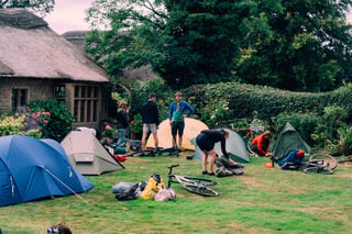Riders pitch tents and unpack bikes on a lawn beside a thatched cottage on the Saturday of the Low Key Lakes Weekender.