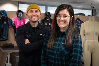 Two smiling people in the Attacus Cycling studio, with cycling jerseys and a tailor's mannequin behind them.
