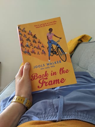 A reader holds the orange paperback of Back in the Frame by Jools Walker on their lap.