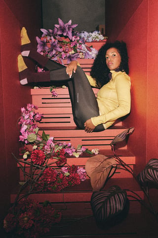 Woman in an I-ris.cc yellow long-sleeve cycling top and dark tights, posed on red stairs among flowers.
