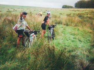 Riders push bikes through long tussocky grass on a Lake District moor during the Low Key Lakes Weekender.