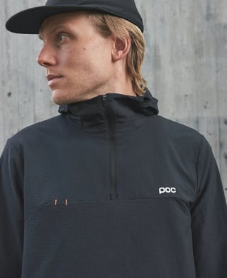 Model in a black cap wearing the POC Mantle thermal hoodie in black, quarter zip and orange stitching visible.