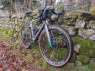 Muddy Chapter2 gravel bike with Scope R4A wheels and a front light against a mossy wall on a wet Deeside Way ride.
