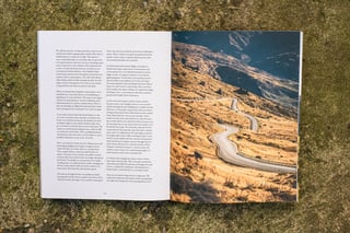 Open Bikepacking Journal spread with text on the left and a photo of a winding road across golden hillsides on the right.