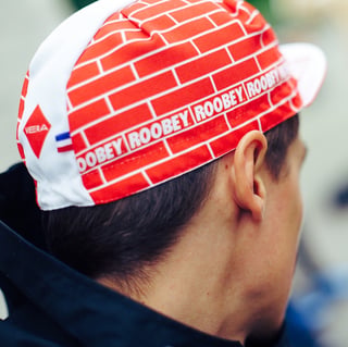 Back of a head in a white and red Vera cycling cap with a brick pattern and repeated Roobey lettering.