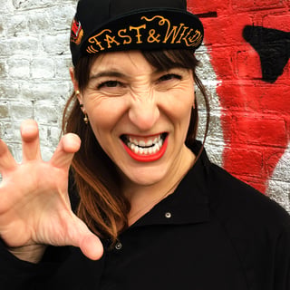 A woman in a black Vera Cycling cap printed Fast &amp; Wild pulls a playful snarl and claws a hand at the camera.