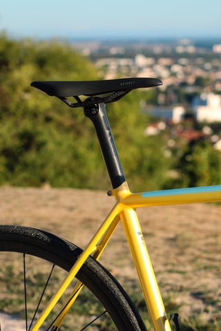 Wish One SUB seat tube junction in yellow with a black seatpost and saddle, a town blurred in the distance.