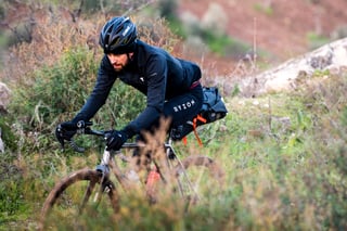 Rider in black Ryzon kit pedals a gravel bike with a saddle pack through scrub on the Jordan Bike Trail.