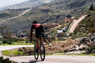 Rider with a saddle pack rides a tarmac road past village houses on a hillside in Jordan.