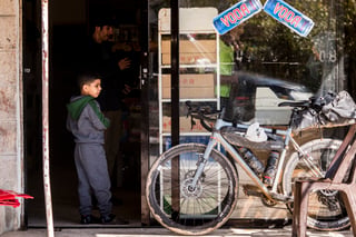 Muddy bikepacking gravel bike parked outside a shop in Jordan while a boy stands in the doorway.