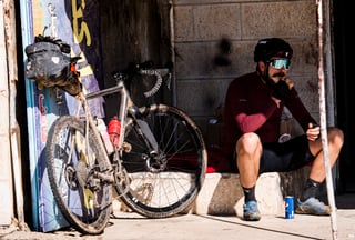 Rider sits on a step eating beside a muddy gravel bike on the Jordan Bike Trail.