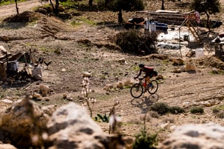 Rider on a gravel bike passes a rural homestead with chickens on a rocky track in Jordan.