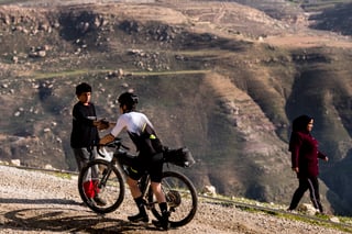 Rider stops on a gravel track above a deep valley in Jordan to shake hands with a young local.