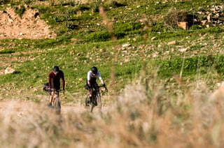 Axel Carion and Jonas Deichmann ride loaded gravel bikes up a stony track through green hillside on the Jordan Bike Trail.
