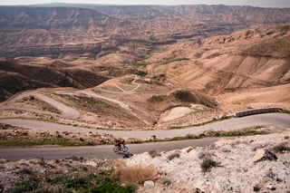 A lone rider descends a switchback road above a wide, dry valley on the Jordan Bike Trail.