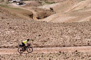 A rider with a handlebar bag and saddle bag pedals a stony desert track in Jordan.