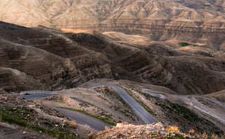 A paved road winds in tight hairpins down a barren hillside in Jordan's dry canyon country.