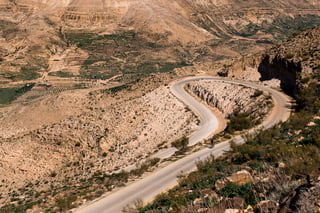 A cyclist is a tiny figure on a hairpin road climbing through terraced hillsides in Jordan.