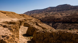 Rocky desert canyon and layered ridgelines under a clear blue sky in Jordan.