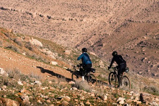 Two bikepackers ride a rocky hillside trail on loaded gravel bikes in Jordan.