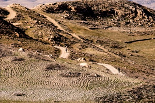Two distant riders follow a dirt track across ploughed, stony hills in Jordan.