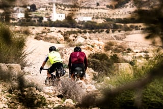 Axel Carion and Jonas Deichmann head along a stony track towards a Jordanian village with a mosque minaret.