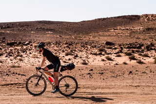 A rider with a saddle bag pedals a gravel bike across rocky desert terrain on the Jordan Bike Trail.