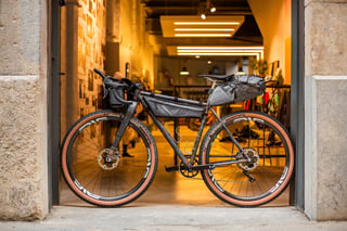 Belle Cycles A.T.E.R. from the non-drive side in a stone shop doorway, with bags on frame, bars and saddle.