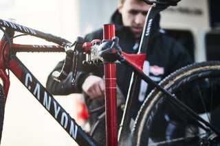Pit mechanic hoses down a Canyon cyclocross bike clamped in a workstand, Dura-Ace levers dripping, at Hoogerheide.