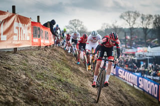 A line of riders climbs a muddy bank at the Hoogerheide Cyclocross World Cup, with Shimano banners trackside.