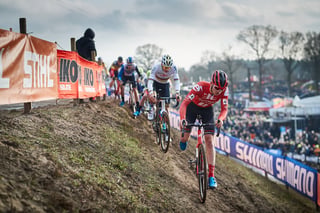 A rider in red leads a single-file line up a rutted bank at Hoogerheide, Mathieu van der Poel on his wheel.