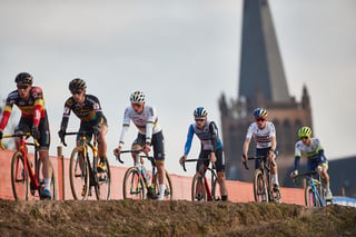 Mathieu van der Poel and five other riders race along a ridge at Hoogerheide, a church spire behind them.
